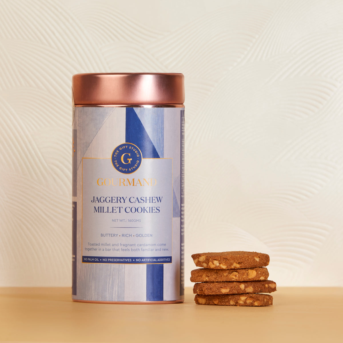 The Gift Studio Gourmand Jaggery Cashew Millet Cookies in a container with a stack of cookies.