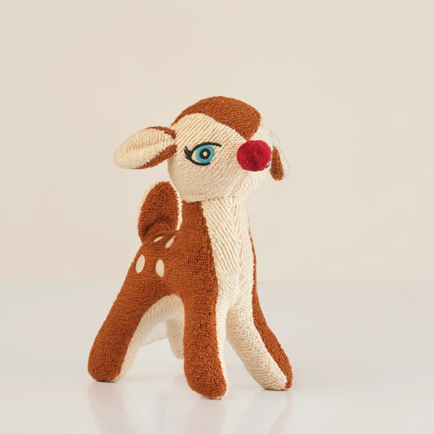 Knitted soft toy deer with red nose, brown and cream colors, and embroidered blue eye