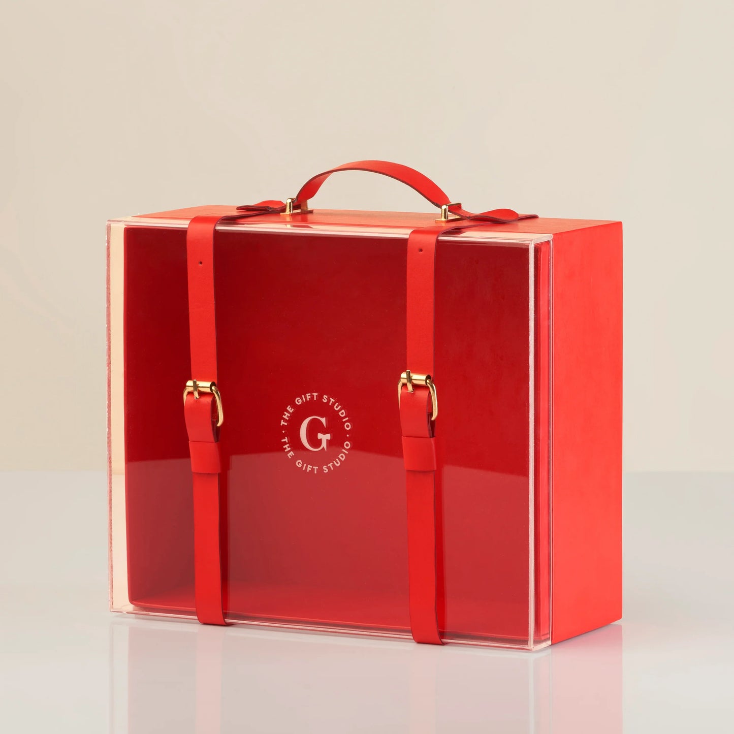 Red acrylic gift box with handle and gold buckled straps, ideal for premium gifting.