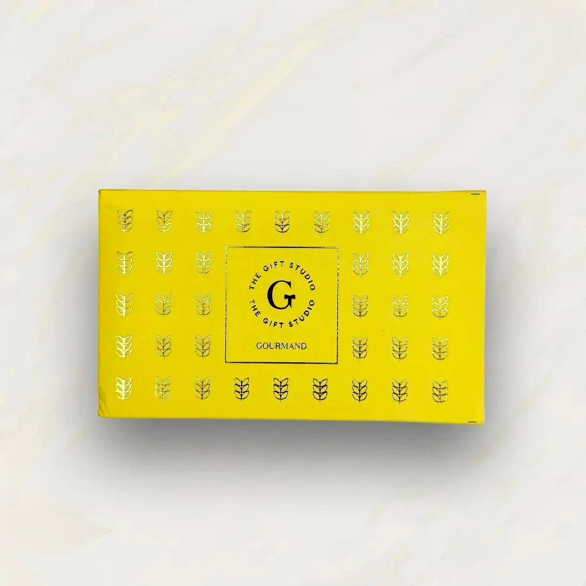 Yellow gift box with gold leaf pattern and 'Gourmand' label on a light background