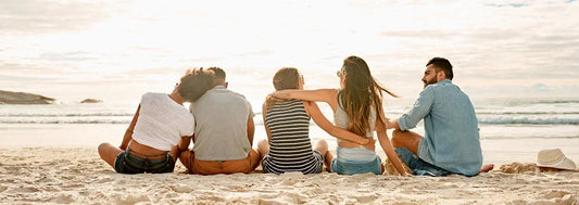 Group of friends sitting on the beach facing the sea, relaxing and enjoying sunny weather