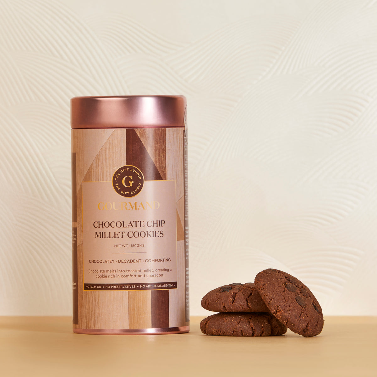 The Gift Studio Gourmand Chocolate Chip Millet Cookies in a rose gold tin with cookies beside it.