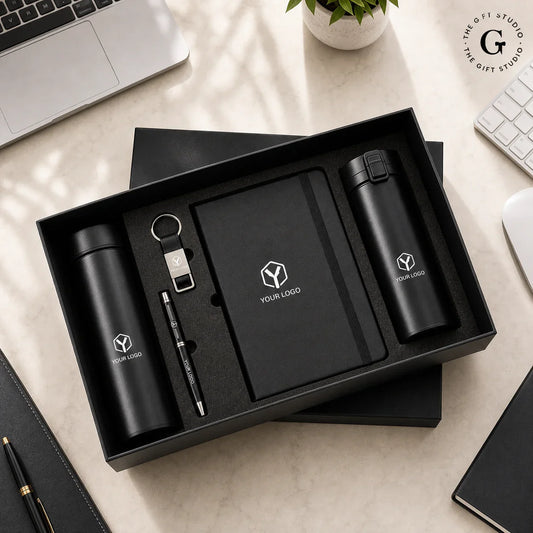 TGS black office gift set with branded items on a wooden surface like pen, bottle, flask, keychain and diary.