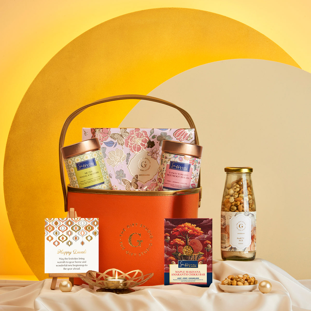 Diwali Floral & Treats Hamper by The Gift Studio featuring gourmet snacks and a greeting card.