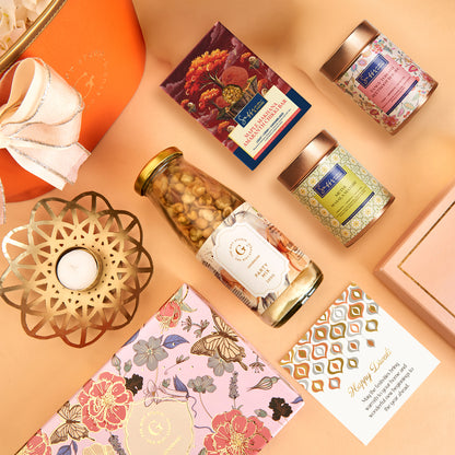 Diwali Floral & Treats Hamper by The Gift Studio with gourmet snacks, tea, and a candle.
