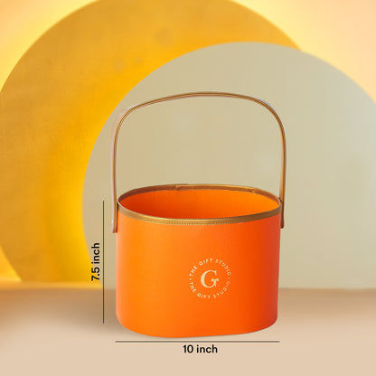 Orange cylindrical gift hamper by The Gift Studio with a gold handle and dimensions.