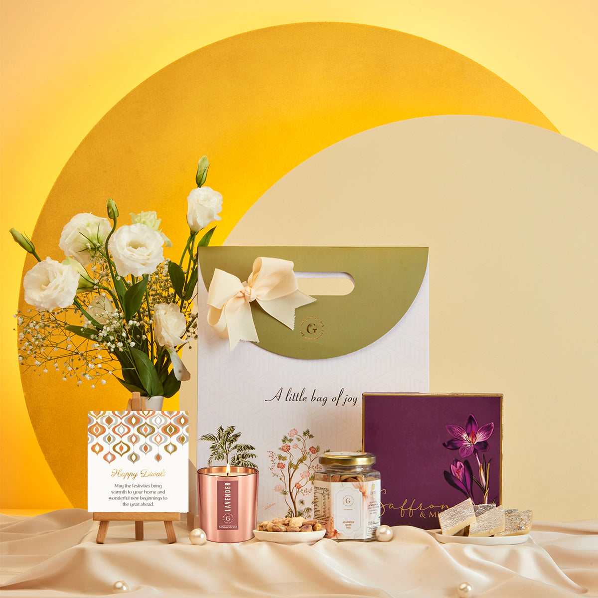 Diwali Radiance Gift Bag by The Gift Studio with candle, sweets, and white flowers.