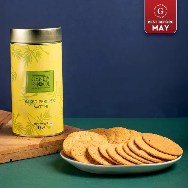 Baked peri peri matthi in a yellow tin with round savory snacks on a white plate