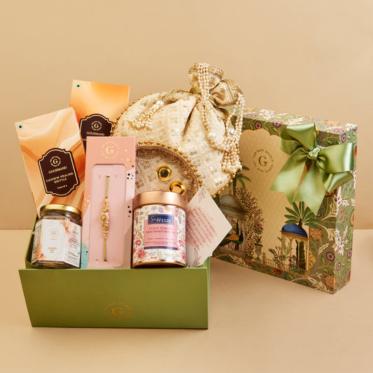 A luxury gift hamper set from the brand  featuring a green presentation box filled with premium items including a gold-embellished drawstring pouch, a Rakhi, and snacks in a gift box.