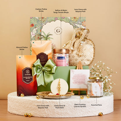 A luxury gift hamper set displayed on a round pedestal against a warm beige background. The set includes a large decorative box with a green bow, a green gift box, a candle, a jar, assorted nuts, and small floral accents.