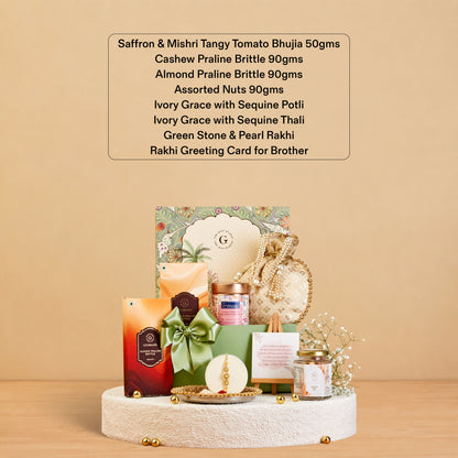 A curated gift set arranged on a round pedestal against a warm beige background, with a text box above listing included items such as saffron, mishti tangy tomato bhuja, cashew praline brittle, almond praline brittle, assorted nuts, ivory grace with sequine thali, green stone & pearl rakhi, and a rakhi greeting card for brother. The set includes packaged food items, a green ribbon, decorative elements, and a small candle.