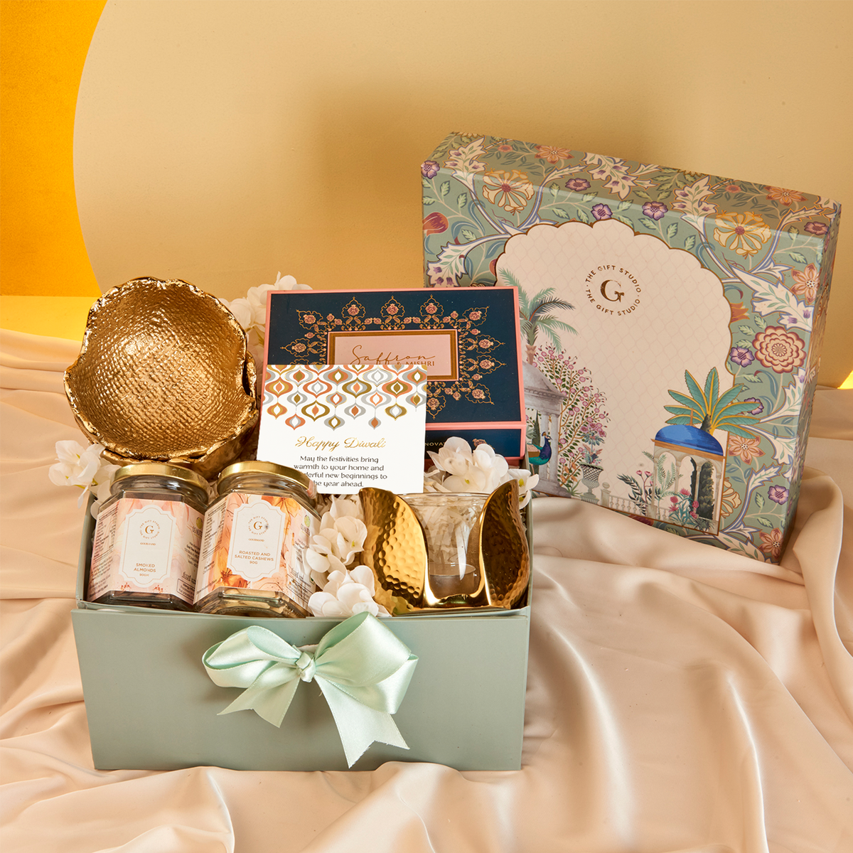 The Diwali Soirée Hamper by The Gift Studio featuring gourmet jars, a gold bowl, and candles.